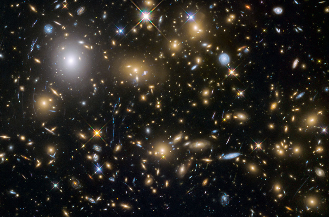 This image from the NASA/ESA Hubble Space Telescope shows the galaxy cluster MACSJ0717.5+3745. This is one of six being studied by the Hubble Frontier Fields programme, which together have produced the deepest images of gravitational lensing ever made. Due to the huge mass of the cluster it is bending the light of background objects, acting as a magnifying lens. It is one of the most massive galaxy clusters known, and it is also the largest known gravitational lens. Of all of the galaxy clusters known and measured, MACS J0717 lenses the largest area of the sky.